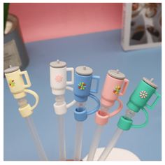 several different colored cups and spoons in a cup on a blue counter top with a pink wall behind them