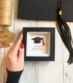 a woman is holding a graduation ornament in a shadow box on a table