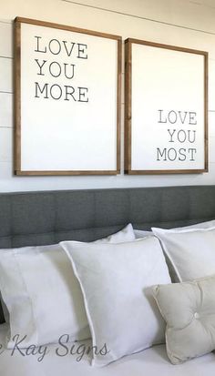 two framed pictures on the wall above a bed with white sheets and pillows, one is saying love you more