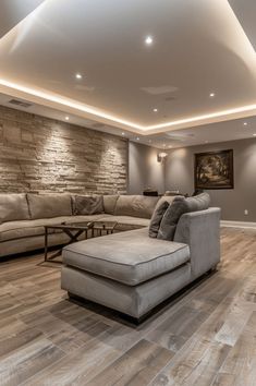 a living room filled with furniture and a stone wall behind the couches, is lit by recessed lights