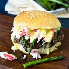 a cheeseburger with asparagus and mayonnaise on a wooden cutting board