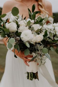 a bride holding a bouquet of white roses and greenery in her hands with the wind