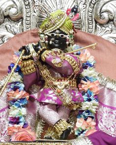 a statue of a hindu god sitting on top of a chair with flowers around it