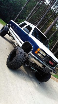 a blue and white truck parked on top of a driveway next to some tall trees