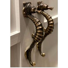 two metal seahorses are attached to the door handle on a white painted wall