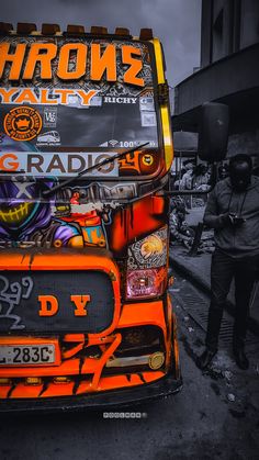 an orange and black double decker bus parked on the side of the road with graffiti all over it