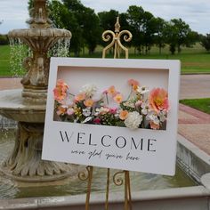 a welcome sign sitting next to a fountain with flowers in the center and a welcome sign below it