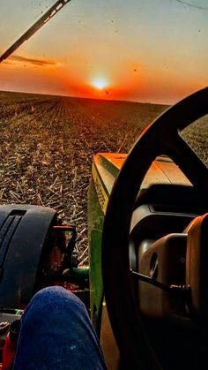 the sun is setting over an open field with tractor equipment in it's foreground