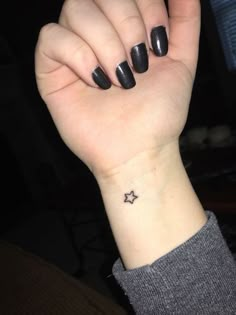 a woman's hand with a small star tattoo on her left wrist and black nails