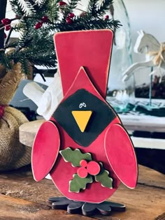 a red and black bird sitting on top of a wooden table next to a christmas tree