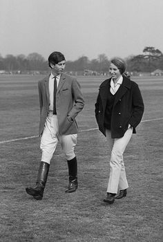 two people standing on top of a grass covered field next to eachother wearing riding boots