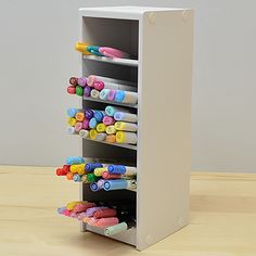 a pen holder with pens and markers in it on top of a wooden table next to a wall