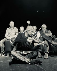 a group of people sitting on top of a floor next to each other playing instruments