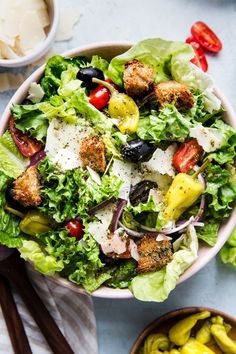 a salad in a bowl with olives, tomatoes and bread croutons on the side