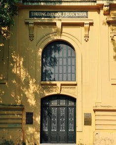 a yellow building with a black door and window on the front side, next to a tree