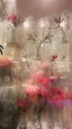 flowers in vases are seen through a window with rain falling on them and behind them is a mirror