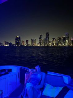 a woman is lounging on the back of a boat in front of a city at night