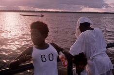 two people standing on a boat in the water with one person wearing a white tank top