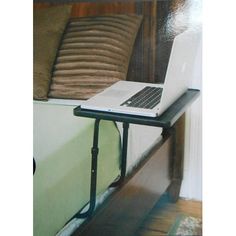 an open laptop computer sitting on top of a metal shelf next to a bed with pillows