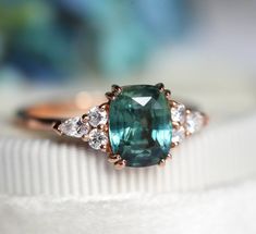 an oval cut green and white diamond ring on top of a white cloth with blue flowers in the background