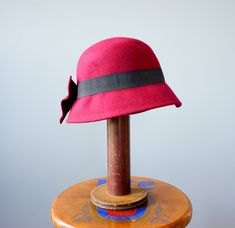 "DESCRIPTION * vintage hat from 1990s * Bucket style: round high crown with sloping downturned stiff brim * made with wool felt fabric * in deep red with a tint of purple * hatband is wrapped with a black grosgrain ribbon and embellished with a red bow * the bow can be worn to the side or to the back * tag reads \"One Size Body 100% Wool, Ribbon 100% Polyester\" CONDITION * Hat is in good clean condition with one spot of the insect bite mark, shown in the last photo. SIZE Hat circumference 22.5\ Vintage Cloche Hat For Winter, Red Vintage Mini Hats With Curved Brim, Vintage Red Adjustable Mini Hats, Red Adjustable Vintage Mini Hats, Vintage Wide Brim Mini Hats For Winter, Vintage Red Fedora Felt Hat, Vintage Red Brimmed Felt Hat, Vintage Red Felt Hat With Short Brim, Vintage Red Felt Hat With Curved Brim