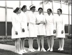 a group of women dressed in white standing next to each other on a sidewalk near a building