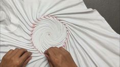 someone is making a spiral design out of white paper on a bed sheet with their hands