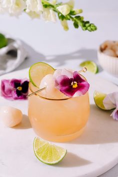 a close up of a drink on a plate with flowers and limes in the background