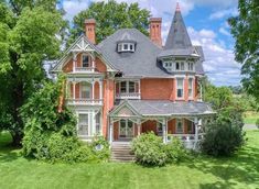 an old red brick house in the middle of a green field with trees and bushes