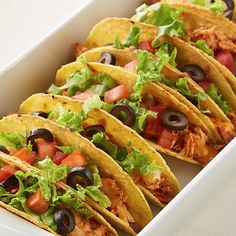 four tacos in a white container with lettuce, tomatoes and black olives