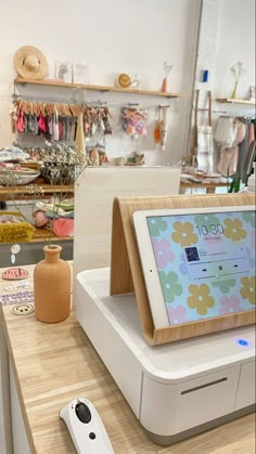 an electronic device sitting on top of a wooden counter next to a vase with flowers