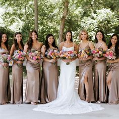 a group of women standing next to each other holding bouquets in front of trees