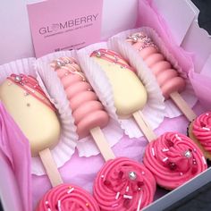 some pink and white cupcakes in a box with candy on sticks next to each other