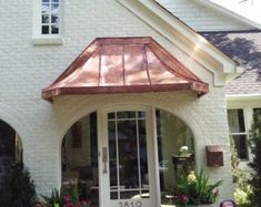 a white brick house with a red copper roof and large glass windows on the front door