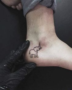 a small elephant tattoo on the foot of a person's left foot, with black gloves