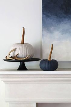 two white pumpkins sitting on top of a black plate next to a blue painting