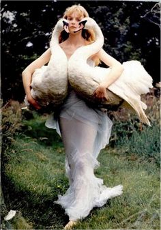 a woman is holding two white birds in her arms while she walks through the grass