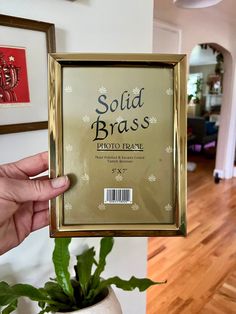 a person holding up a gold framed photo in front of a potted green plant