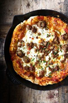 a pizza with meatballs and cheese in a skillet on a wooden table top