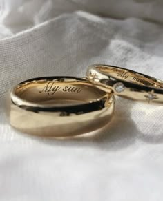 two gold wedding rings with the words my sun written on them sitting on a white cloth