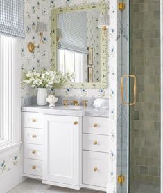 a white bathroom with floral wallpaper and gold hardware on the vanity, along with a walk in shower