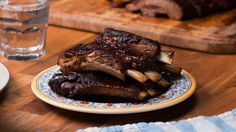 a plate with some ribs on it next to a glass of water and a cutting board