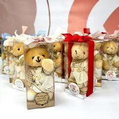 four small teddy bears in clear boxes with red bows on them, sitting next to each other