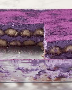 a cake with purple frosting on it sitting on a counter next to a knife