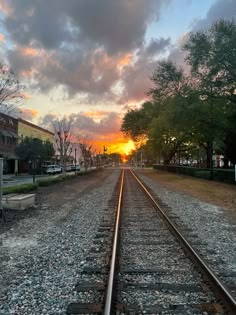 the sun is setting on an empty train track in front of some buildings and trees