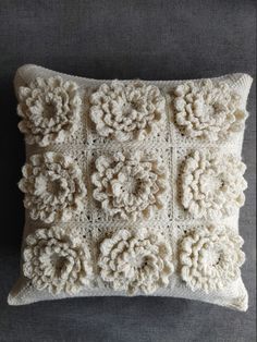 a white crocheted pillow with flowers on the front and sides, sitting on a gray surface