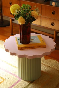 a vase with flowers sitting on top of a table next to a book and a dresser