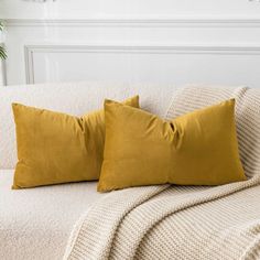 two yellow pillows sitting on top of a white couch next to a potted plant