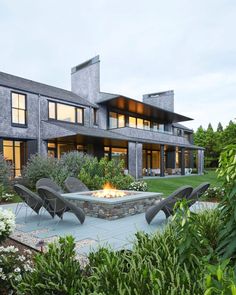 an outdoor fire pit in front of a large house with lots of windows and plants