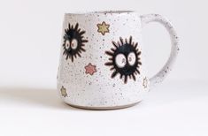 a white coffee mug with black eyes and stars painted on the side, sitting against a white background